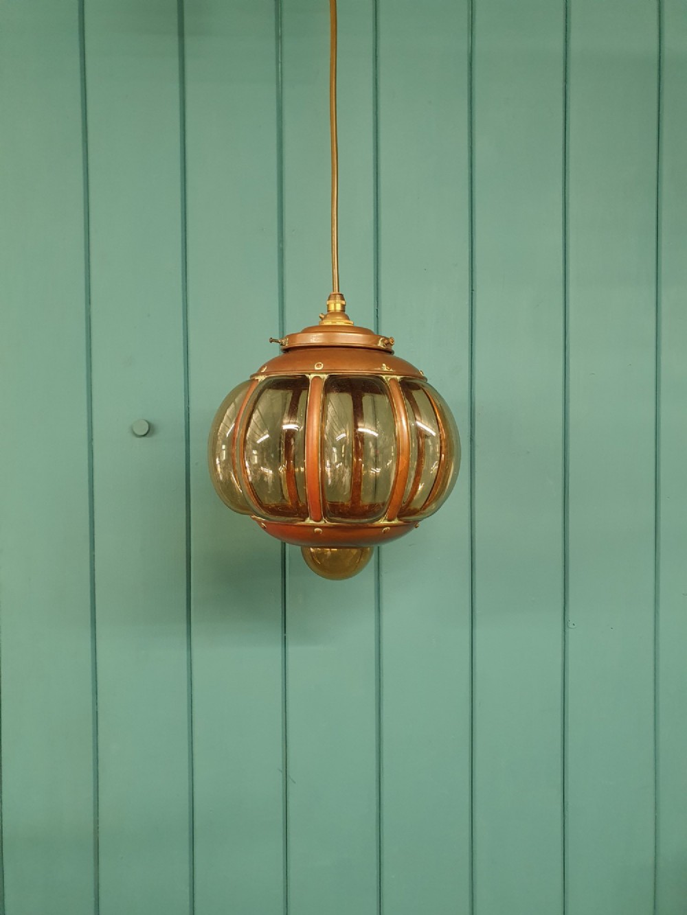 A spherical nautical pendant light featuring a copper cap and framed body enclosing a ribbed smoked amber glass globe.