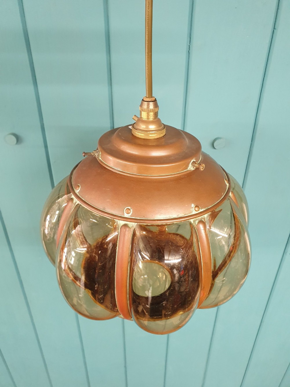 A spherical nautical pendant light featuring a copper cap and framed body enclosing a ribbed smoked amber glass globe. View V