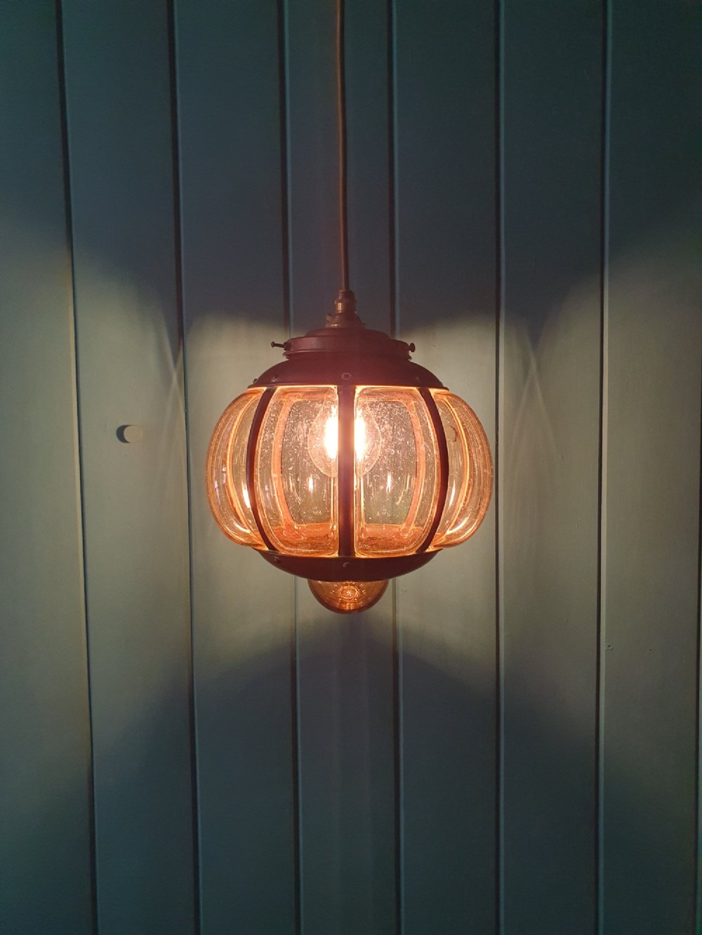 A spherical nautical pendant light featuring a copper cap and framed body enclosing a ribbed smoked amber glass globe. View VI