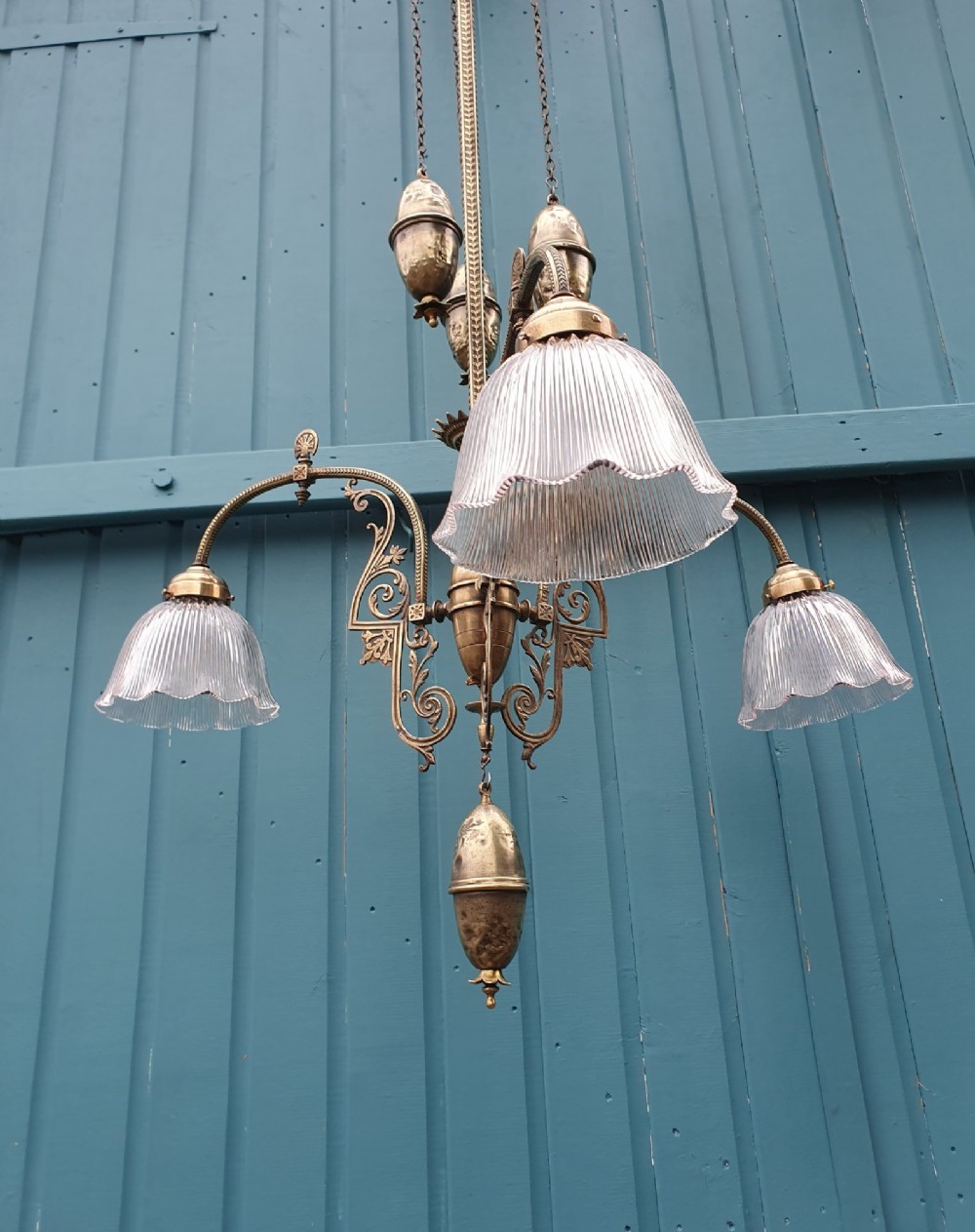 An antique brass three-arm rise and fall chandelier with fluted clear glass shades and scrolled metalwork detailing. View III