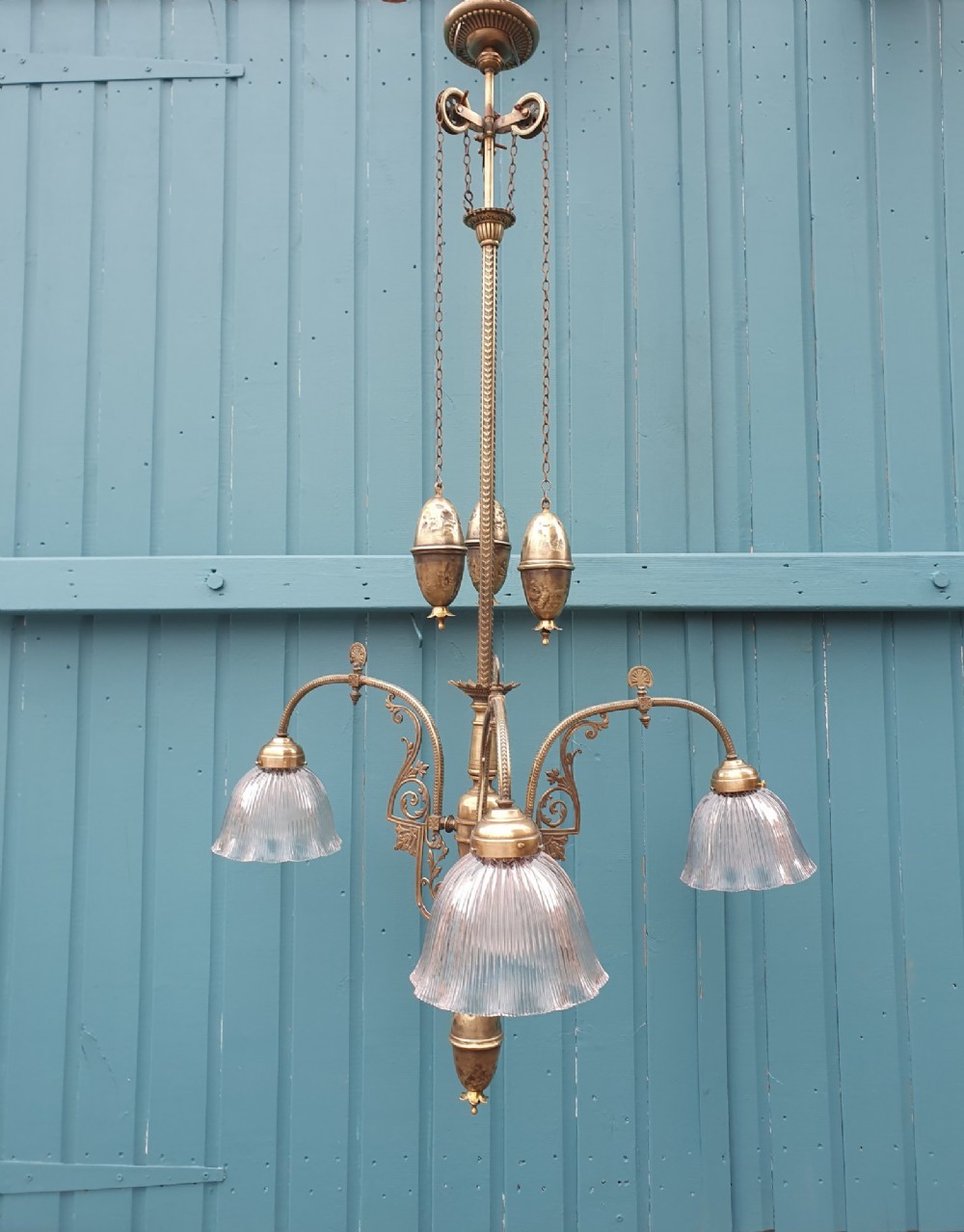 An antique brass three-arm rise and fall chandelier with fluted clear glass shades and scrolled metalwork detailing.