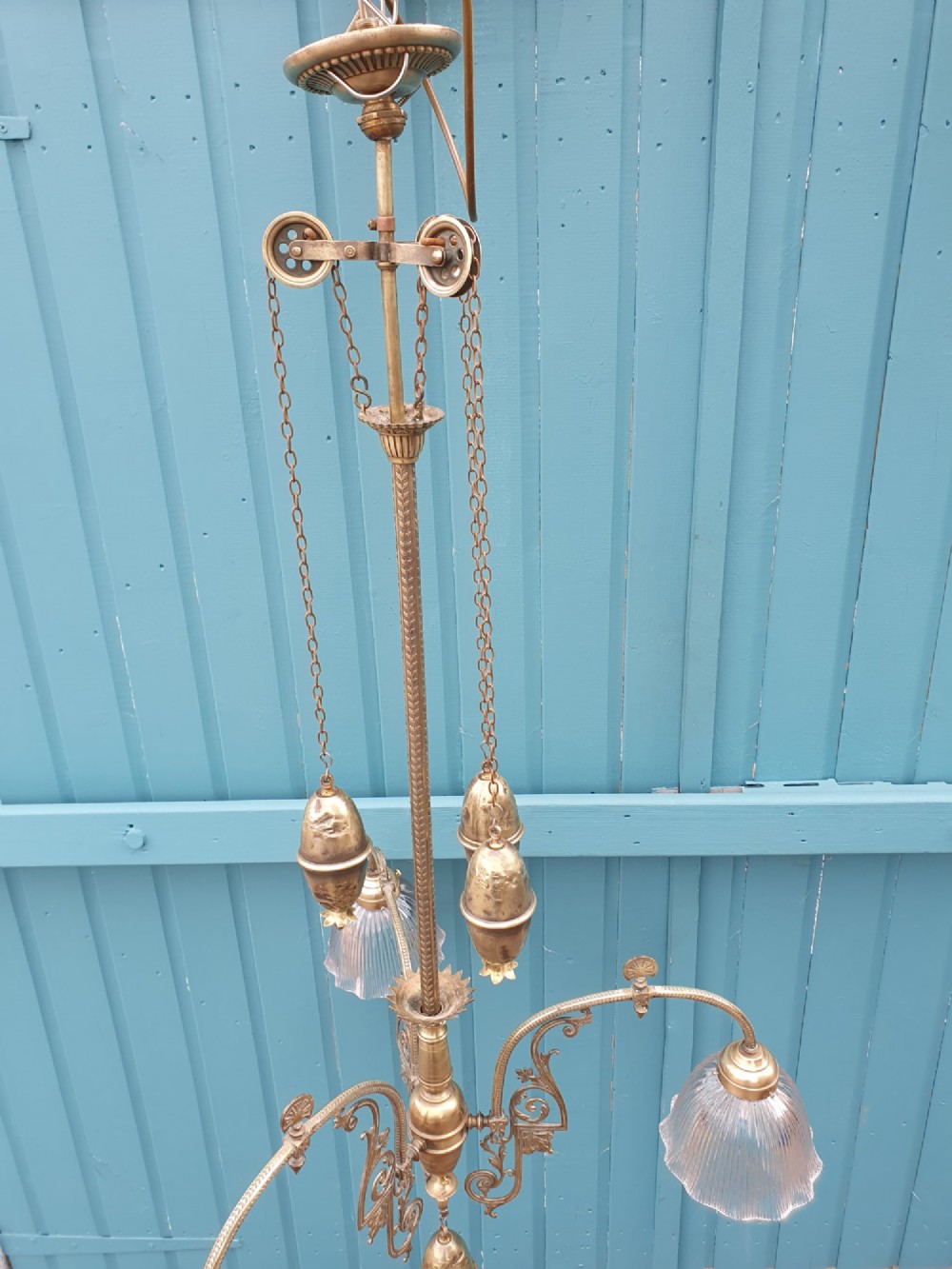 An antique brass three-arm rise and fall chandelier with fluted clear glass shades and scrolled metalwork detailing. View VII