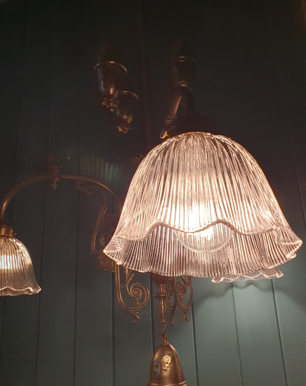 An antique brass three-arm rise and fall chandelier with fluted clear glass shades and scrolled metalwork detailing. View VIII