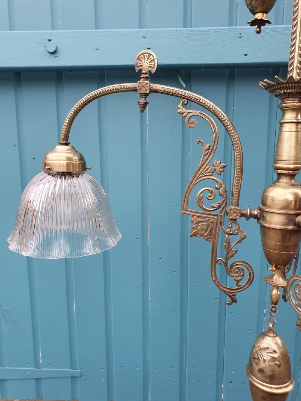 An antique brass three-arm rise and fall chandelier with fluted clear glass shades and scrolled metalwork detailing. View X