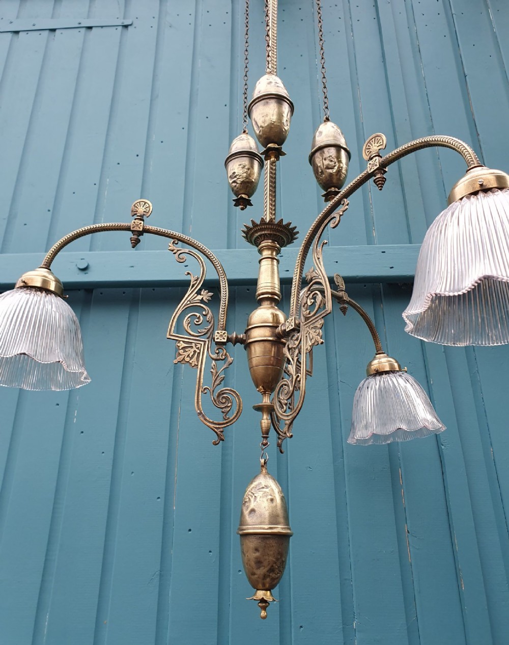 An antique brass three-arm rise and fall chandelier with fluted clear glass shades and scrolled metalwork detailing. View XII