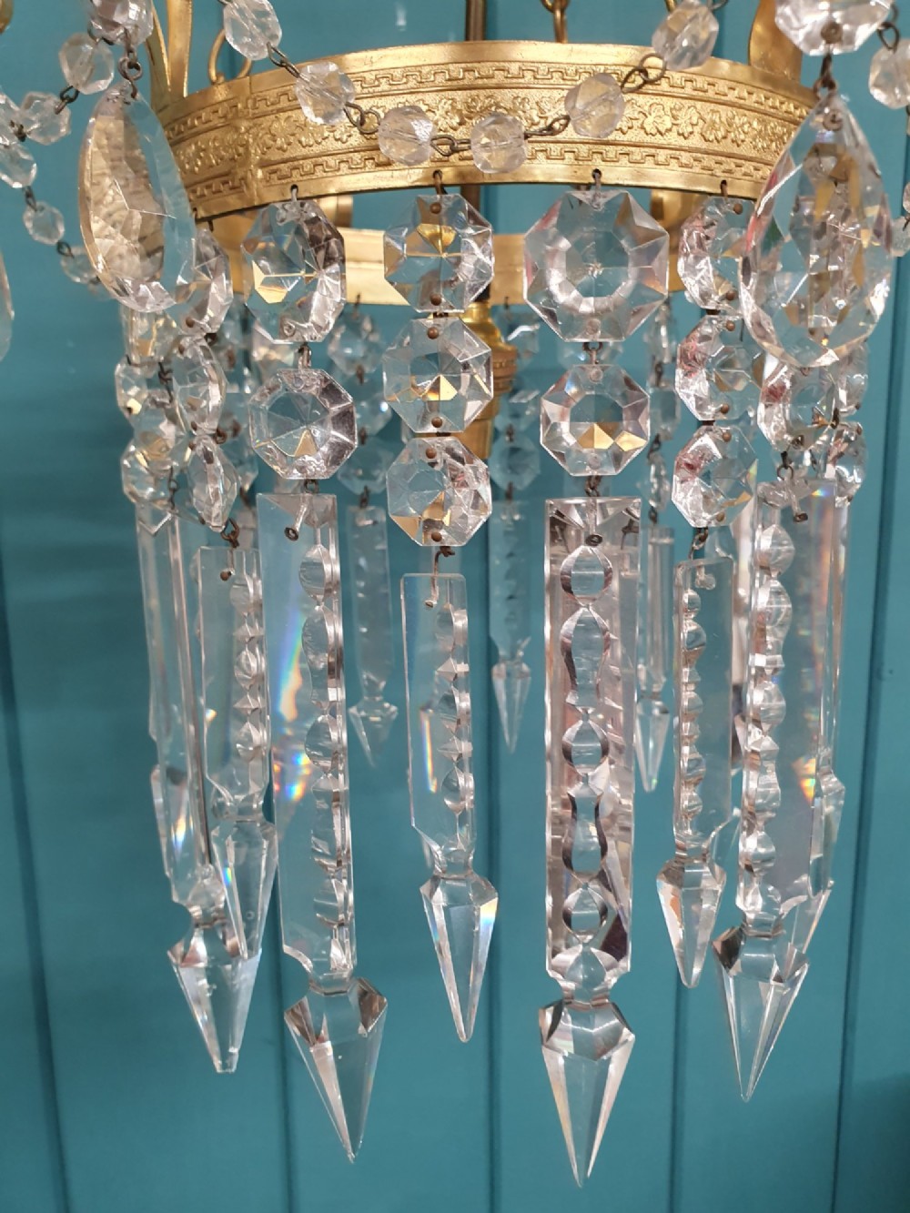 An antique ceiling chandelier featuring a brass metal frame with top scrollwork and tiered cut glass spike prisms hanging down. View II