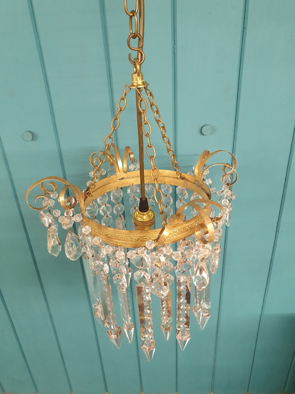 An antique ceiling chandelier featuring a brass metal frame with top scrollwork and tiered cut glass spike prisms hanging down. View III