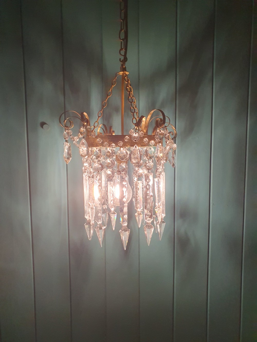 An antique ceiling chandelier featuring a brass metal frame with top scrollwork and tiered cut glass spike prisms hanging down. View IV