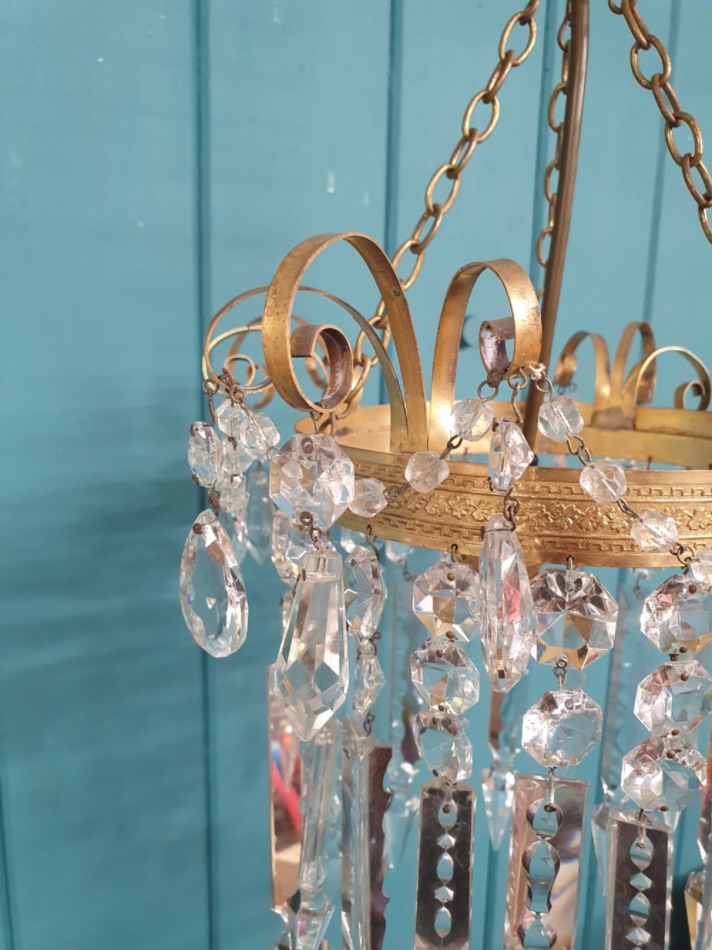 An antique ceiling chandelier featuring a brass metal frame with top scrollwork and tiered cut glass spike prisms hanging down. View V