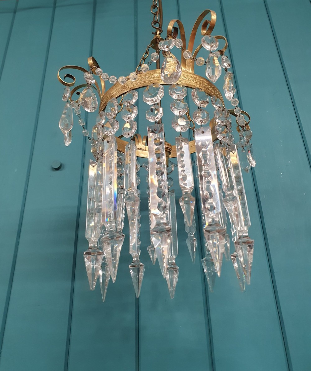 An antique ceiling chandelier featuring a brass metal frame with top scrollwork and tiered cut glass spike prisms hanging down. View VI