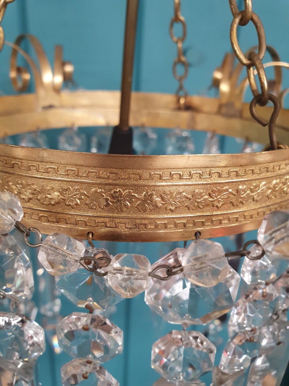 An antique ceiling chandelier featuring a brass metal frame with top scrollwork and tiered cut glass spike prisms hanging down. View VII