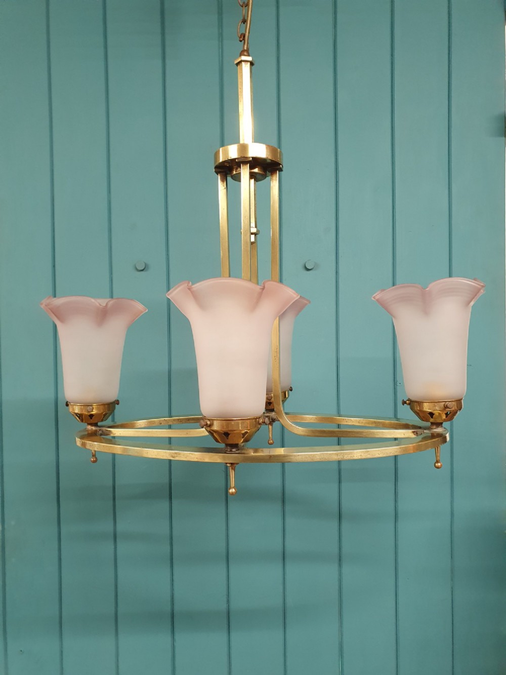 An Art Deco brass four-light chandelier featuring a circular brass frame suspending four tulip-shaped pink frosted glass shades with ruffled rims.