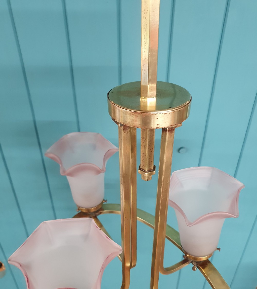 An Art Deco brass four-light chandelier featuring a circular brass frame suspending four tulip-shaped pink frosted glass shades with ruffled rims. View V