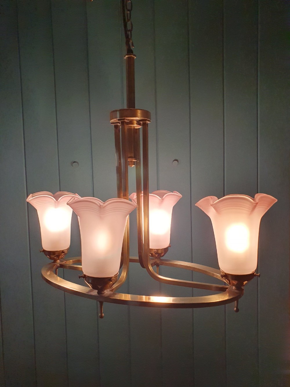 An Art Deco brass four-light chandelier featuring a circular brass frame suspending four tulip-shaped pink frosted glass shades with ruffled rims. View VII