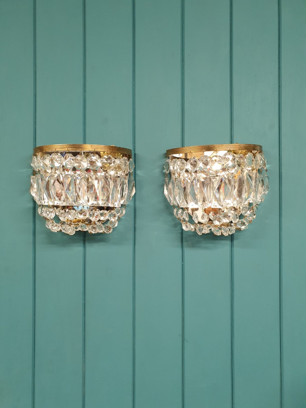 A pair of early 20th-century wall sconces featuring semi-circular brass frames hung with tiered cut-crystal prisms.