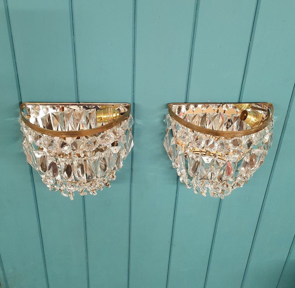 A pair of early 20th-century wall sconces featuring semi-circular brass frames hung with tiered cut-crystal prisms. View VI
