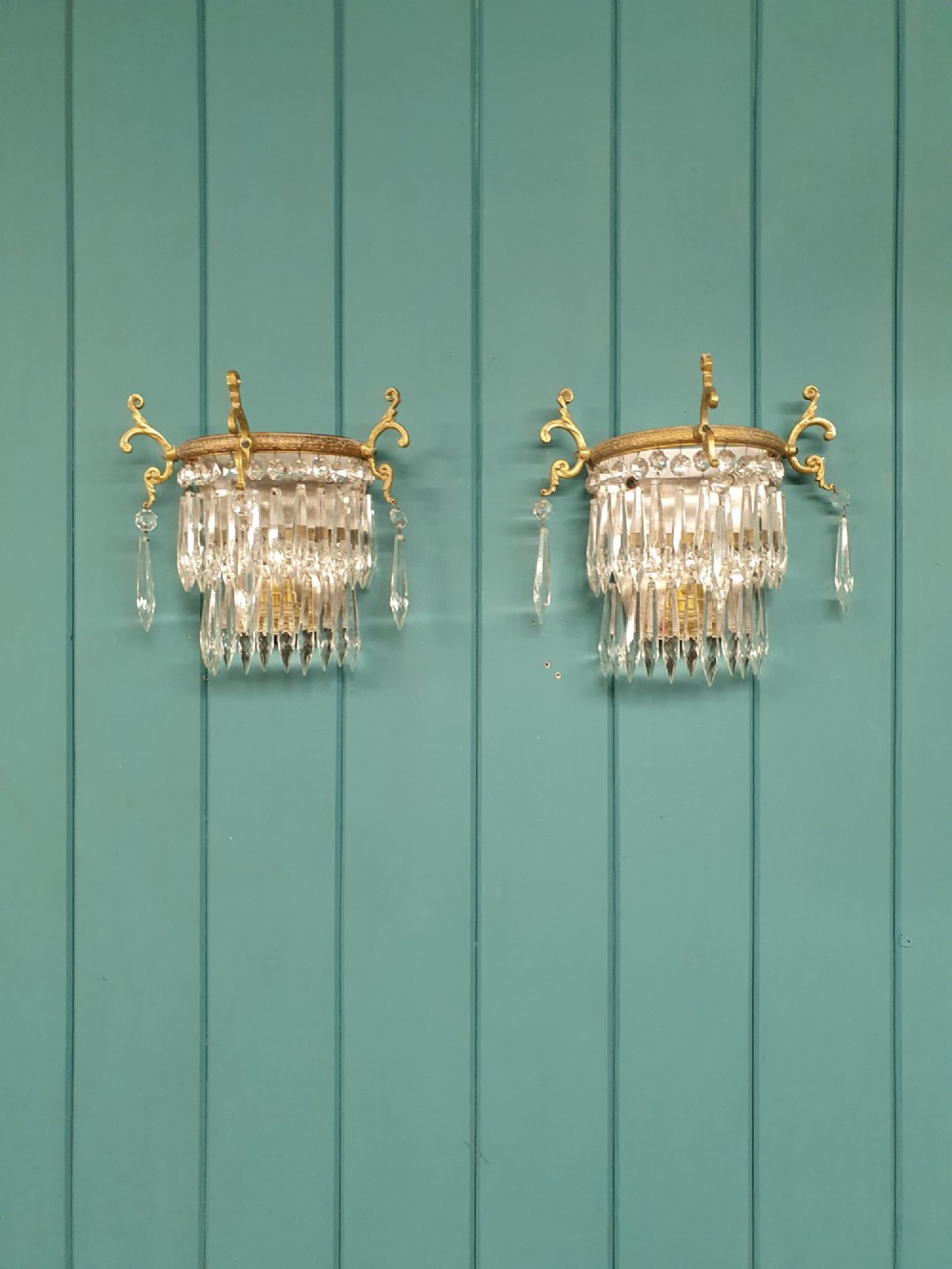 A pair of antique gilt brass wall lights featuring cascading concentric tiers of pointed crystal glass prisms.