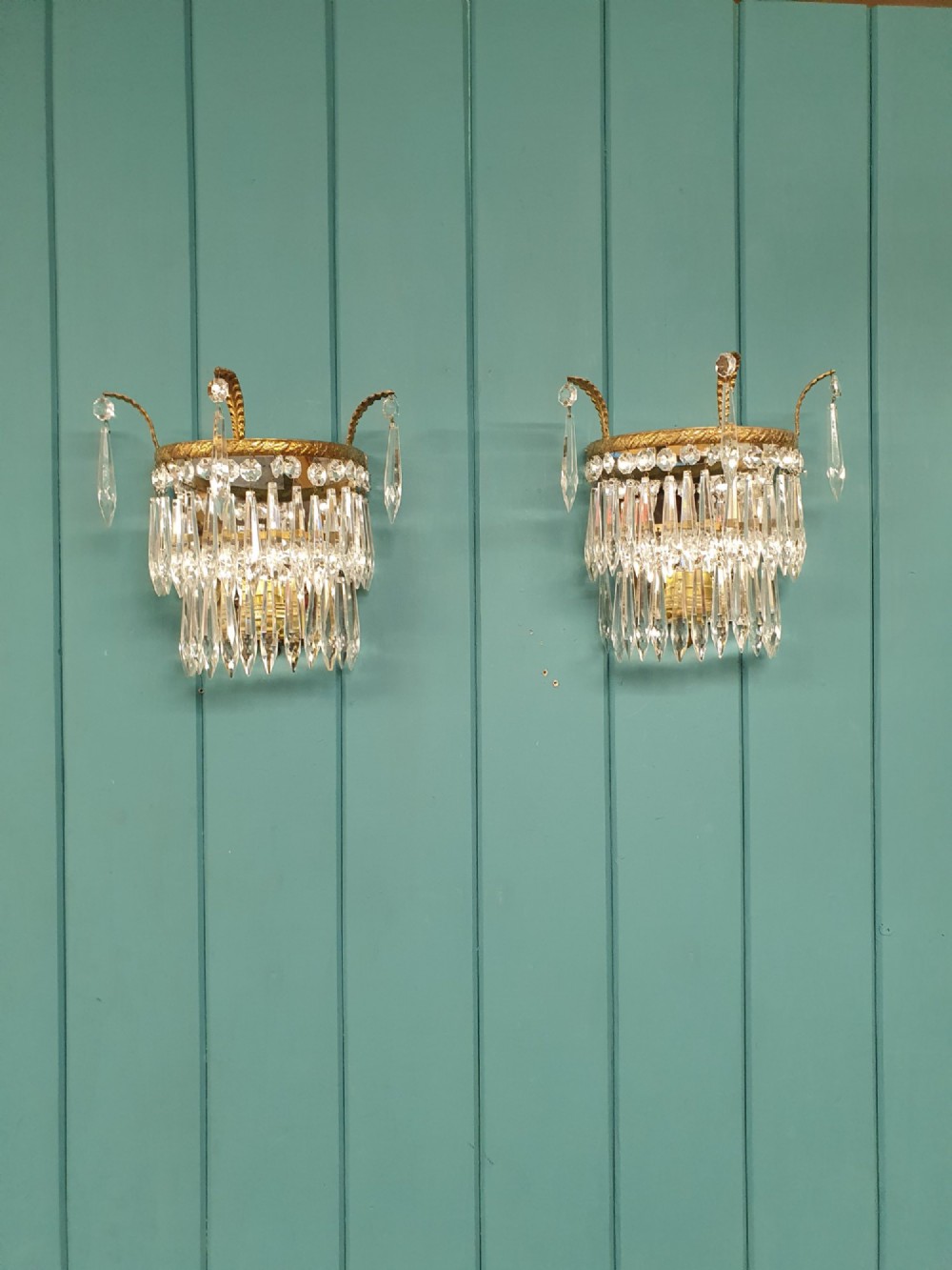 A pair of antique gilt brass wall lights adorned with cascading tiers of crystal spikes and glass drops.