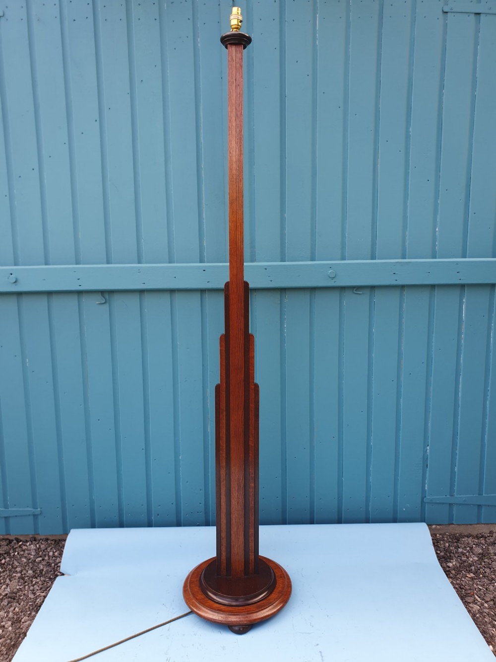 An Art Deco wooden standard lamp featuring a stepped skyscraper column design set upon a circular turned base with a brass light fitting.