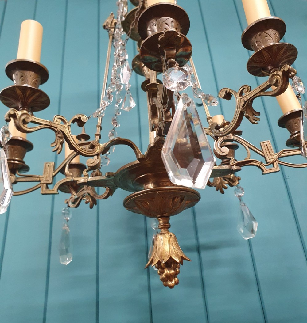 An antique eight-arm brass chandelier decorated with cut crystal drops, faceted beads, and cast lion mask details. View II