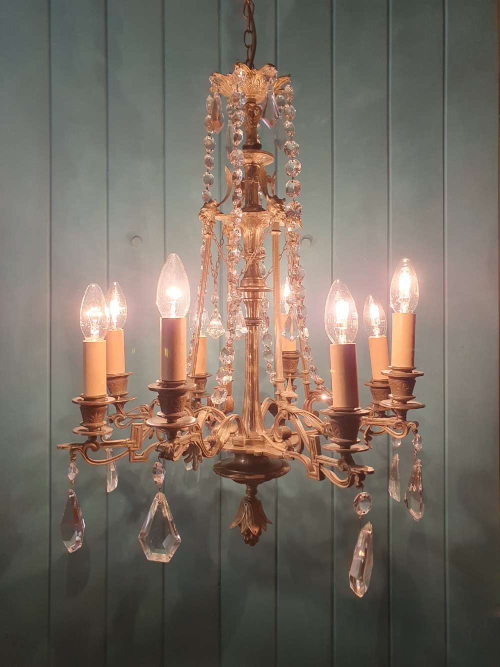 An antique eight-arm brass chandelier decorated with cut crystal drops, faceted beads, and cast lion mask details. View III