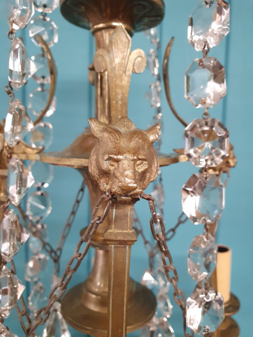 An antique eight-arm brass chandelier decorated with cut crystal drops, faceted beads, and cast lion mask details. View IV