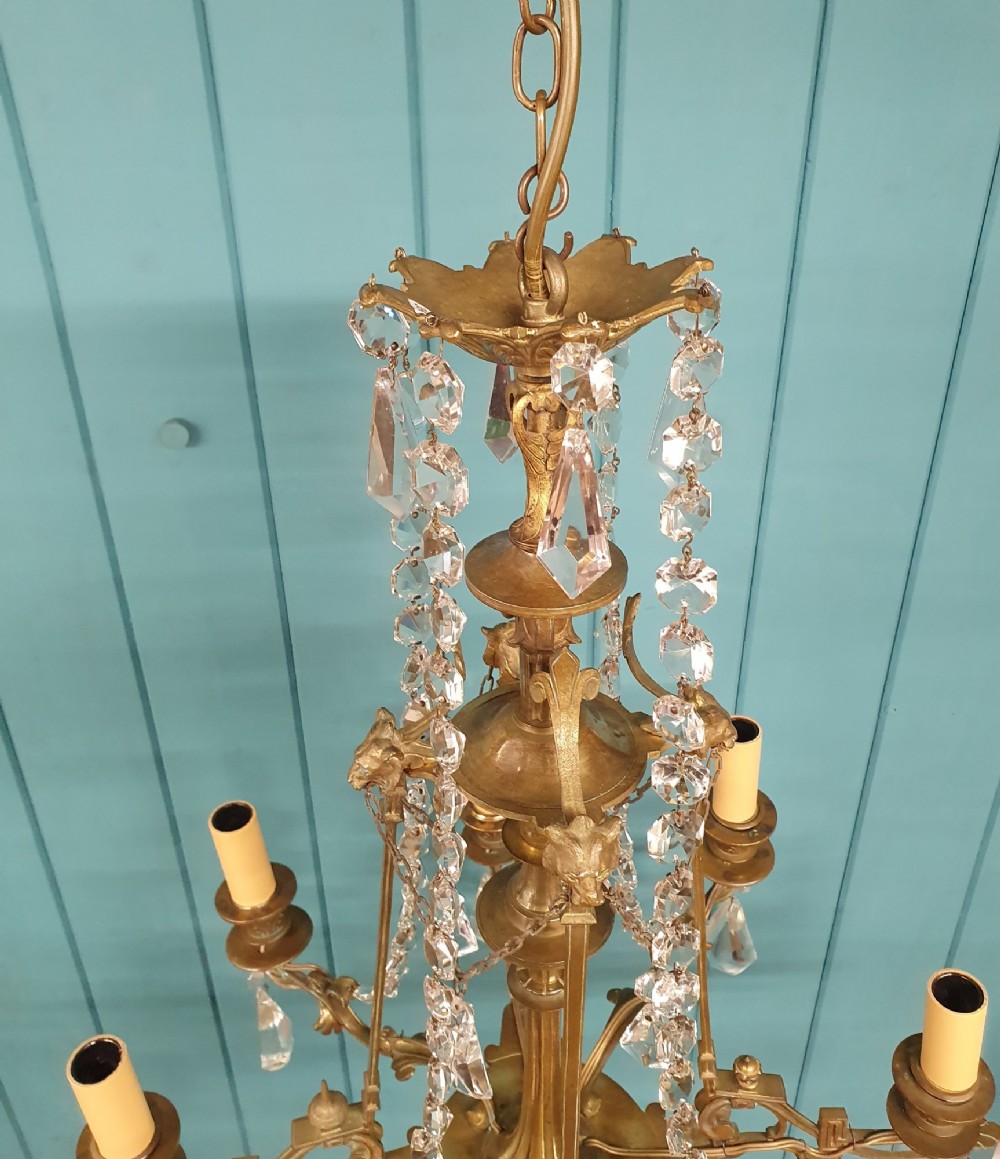 An antique eight-arm brass chandelier decorated with cut crystal drops, faceted beads, and cast lion mask details. View V