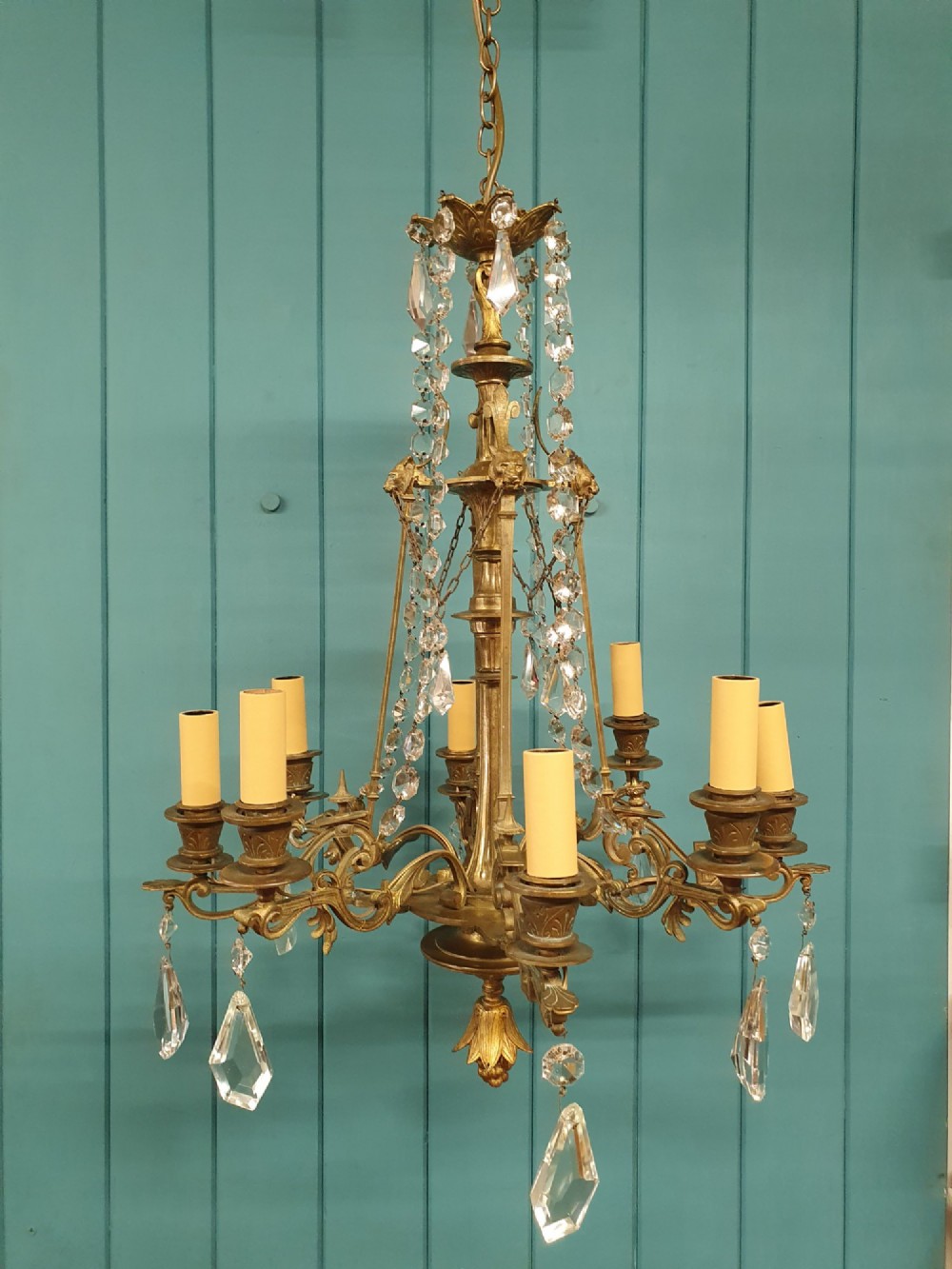 An antique eight-arm brass chandelier decorated with cut crystal drops, faceted beads, and cast lion mask details. View VI