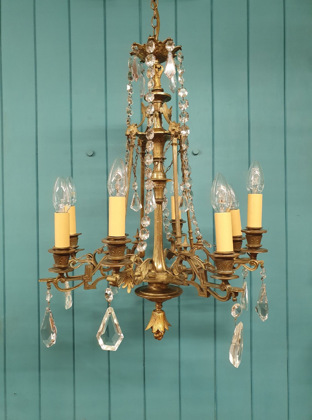 An antique eight-arm brass chandelier decorated with cut crystal drops, faceted beads, and cast lion mask details.