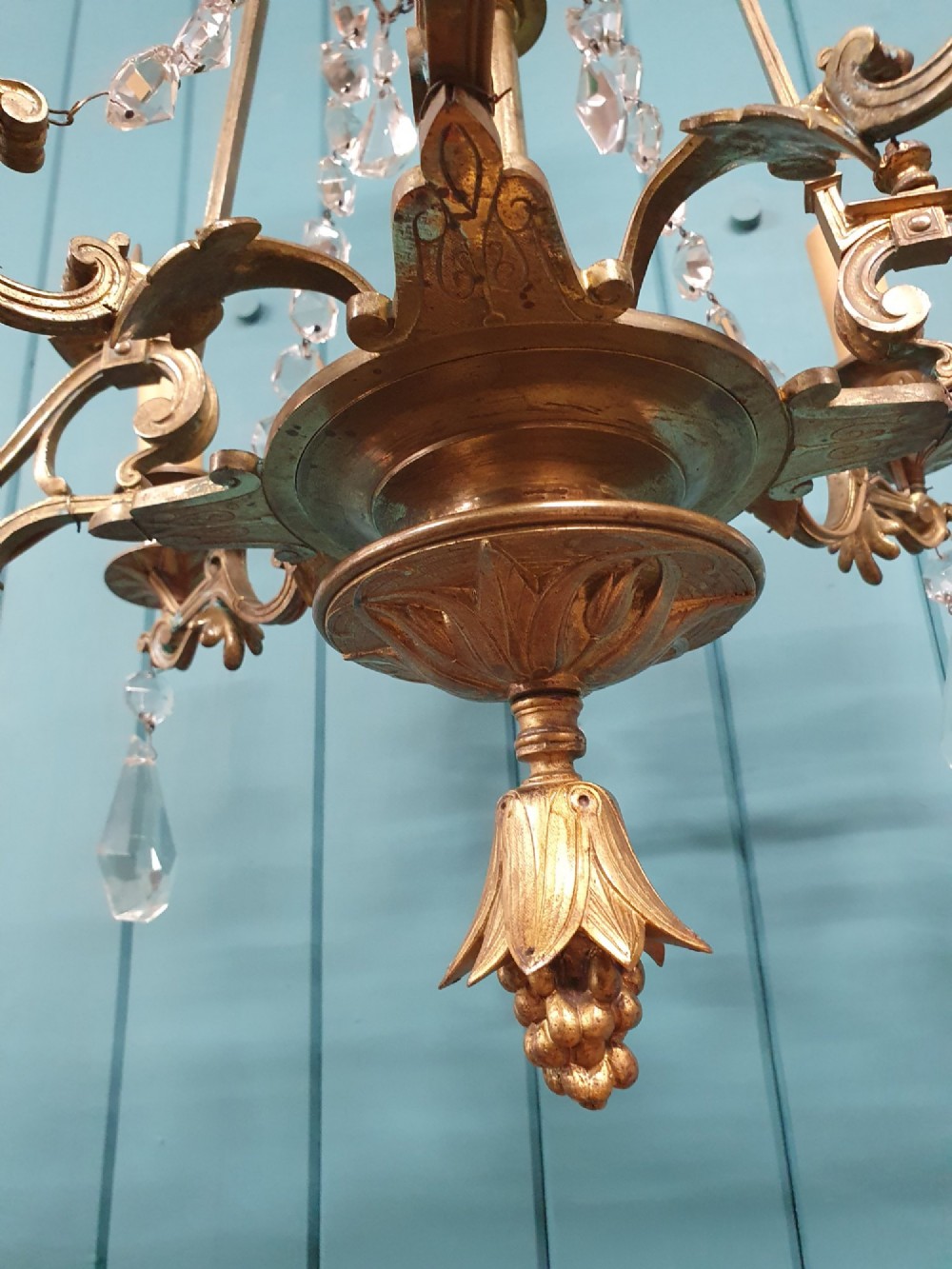 An antique eight-arm brass chandelier decorated with cut crystal drops, faceted beads, and cast lion mask details. View IX
