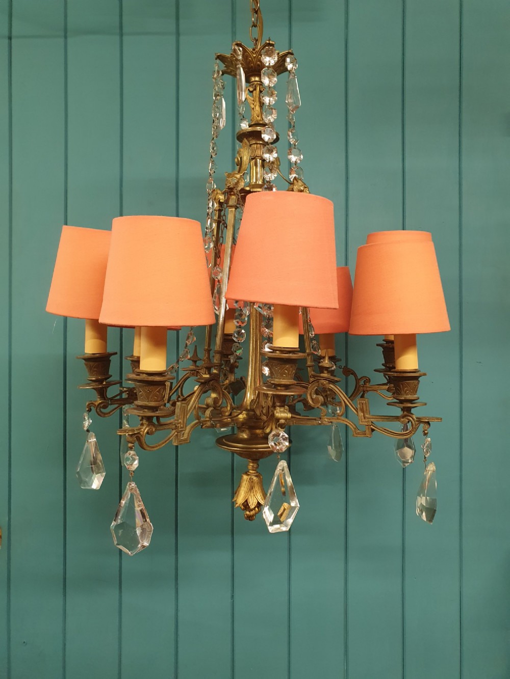 An antique eight-arm brass chandelier decorated with cut crystal drops, faceted beads, and cast lion mask details. View X