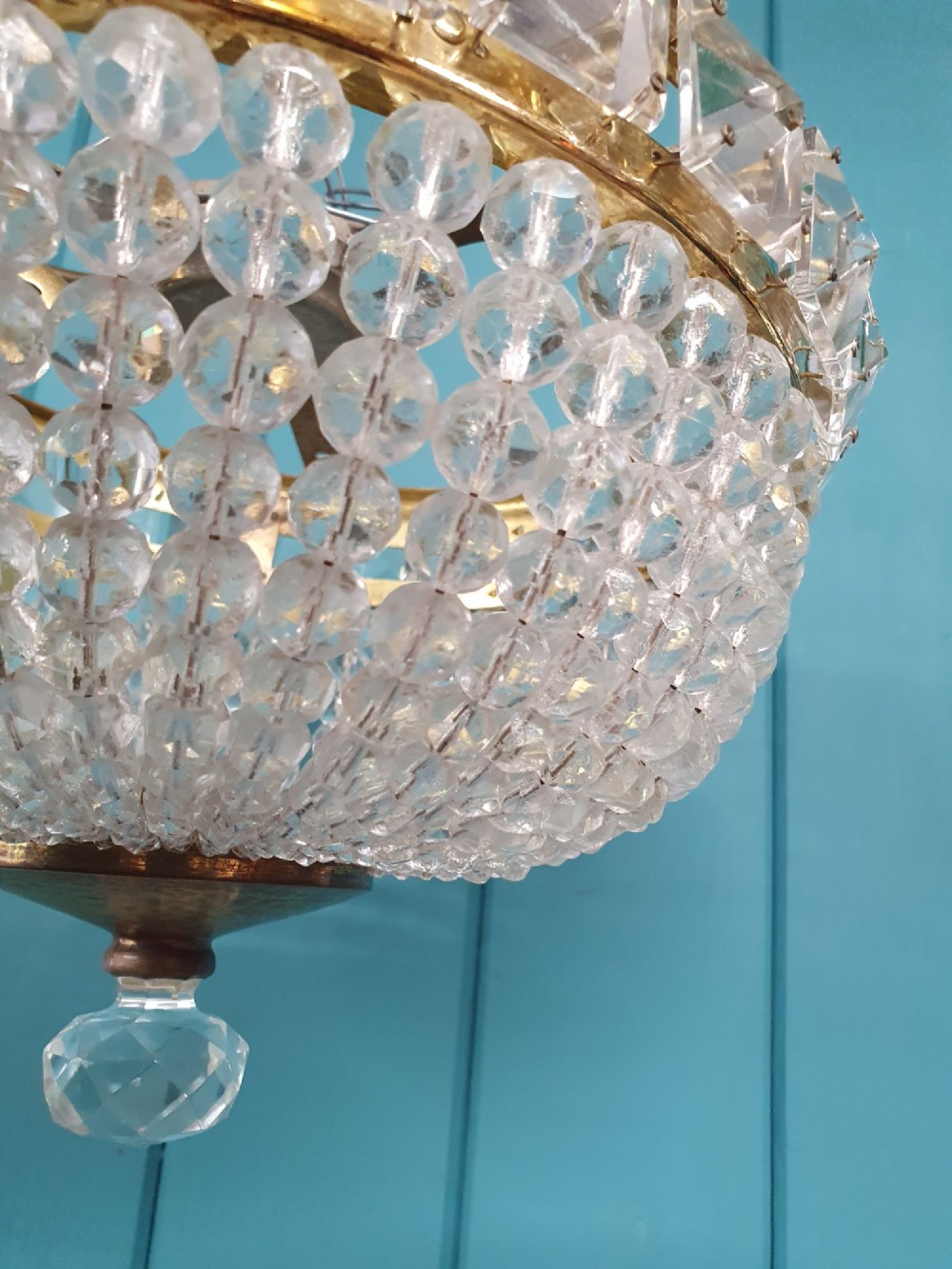 An early twentieth-century ceiling chandelier featuring a brass rim set with rectangular cut-glass prisms and a tapered bowl formed of clear glass beads ending in a faceted finial. View II