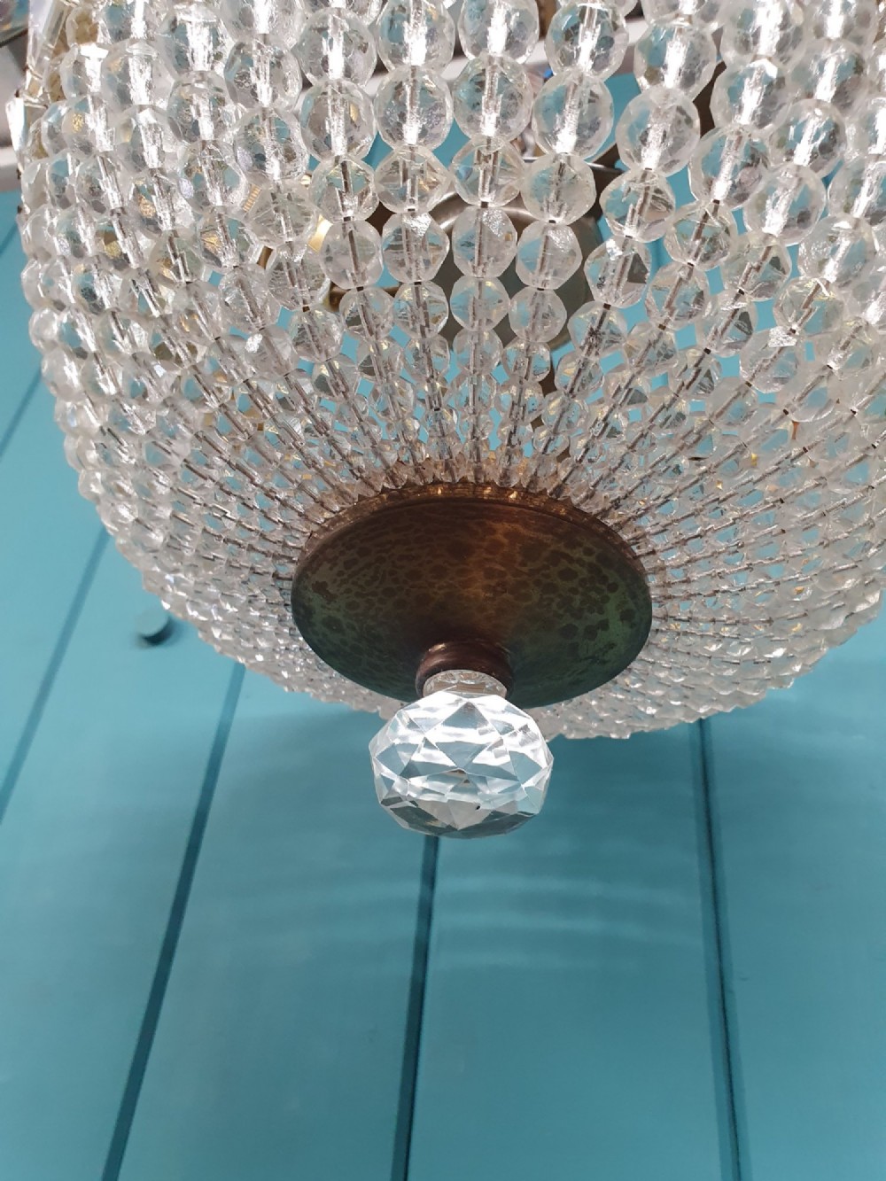 An early twentieth-century ceiling chandelier featuring a brass rim set with rectangular cut-glass prisms and a tapered bowl formed of clear glass beads ending in a faceted finial. View IV