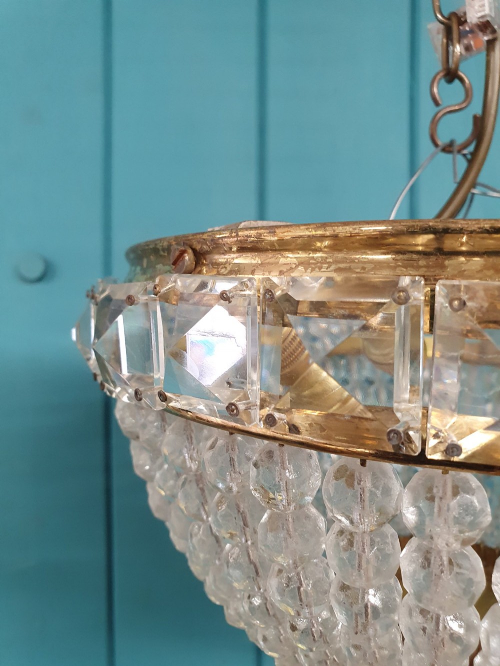 An early twentieth-century ceiling chandelier featuring a brass rim set with rectangular cut-glass prisms and a tapered bowl formed of clear glass beads ending in a faceted finial. View V