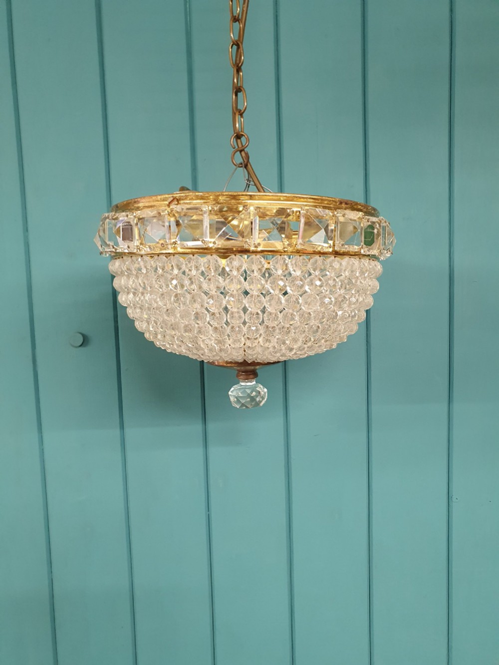 An early twentieth-century ceiling chandelier featuring a brass rim set with rectangular cut-glass prisms and a tapered bowl formed of clear glass beads ending in a faceted finial.