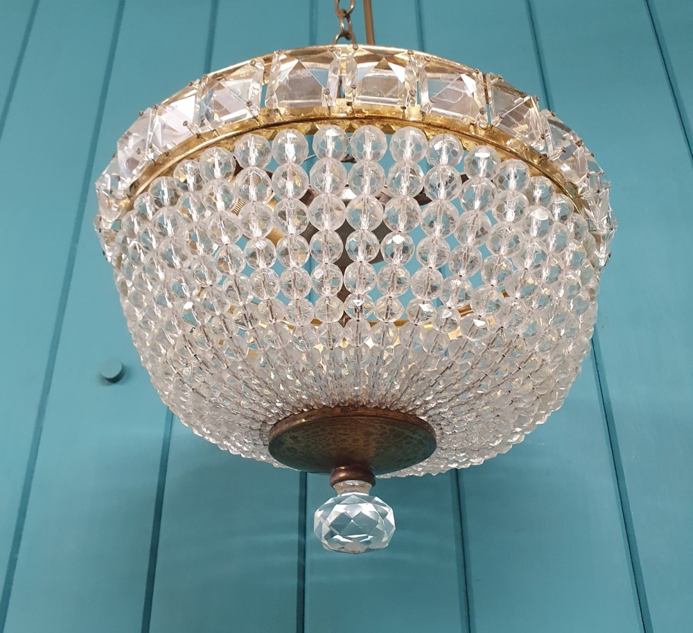 An early twentieth-century ceiling chandelier featuring a brass rim set with rectangular cut-glass prisms and a tapered bowl formed of clear glass beads ending in a faceted finial. View VI
