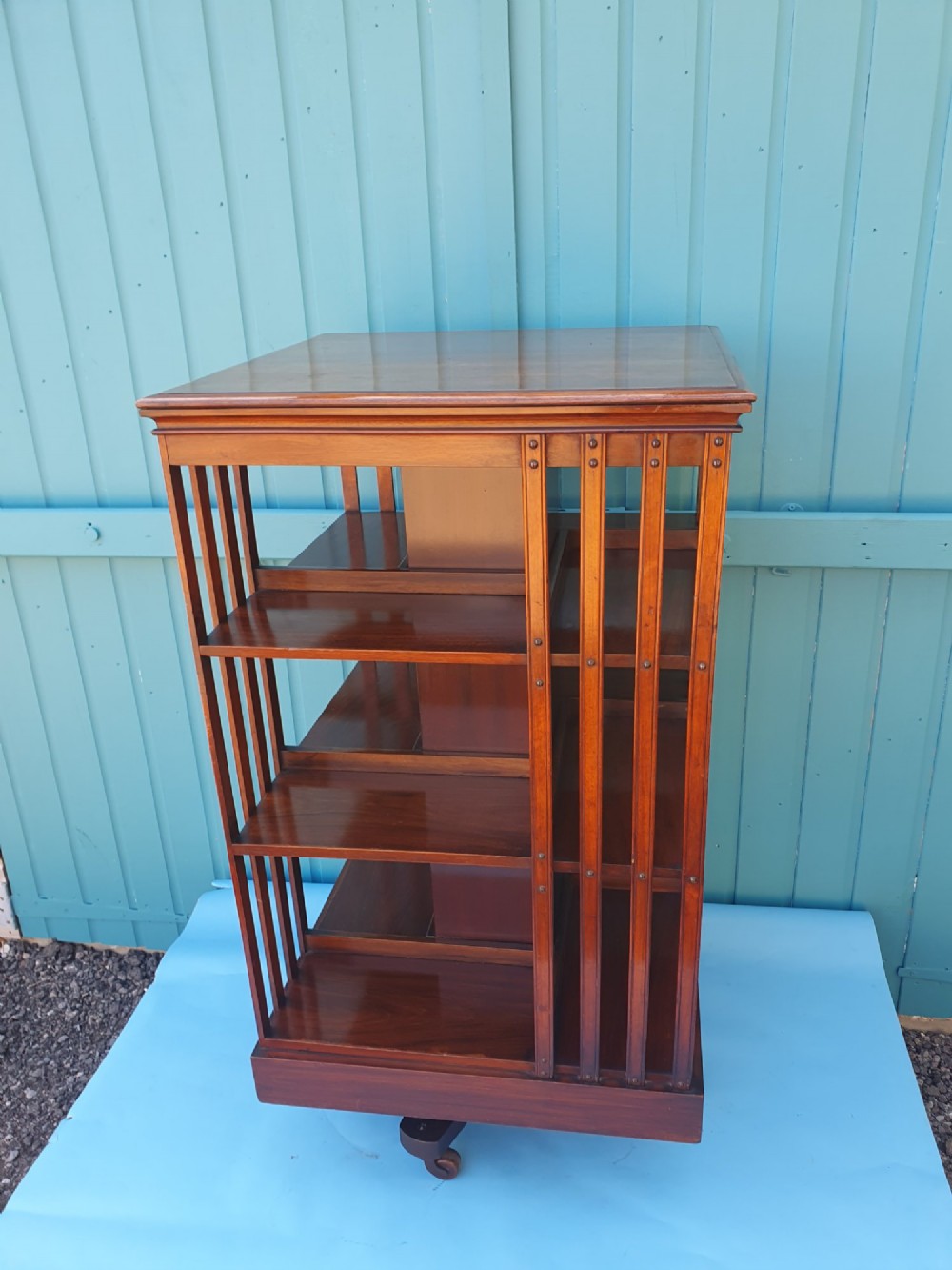 A four-tiered Victorian walnut revolving bookcase featuring vertical slatted sides, open shelf compartments, and a square moulded top on castors.