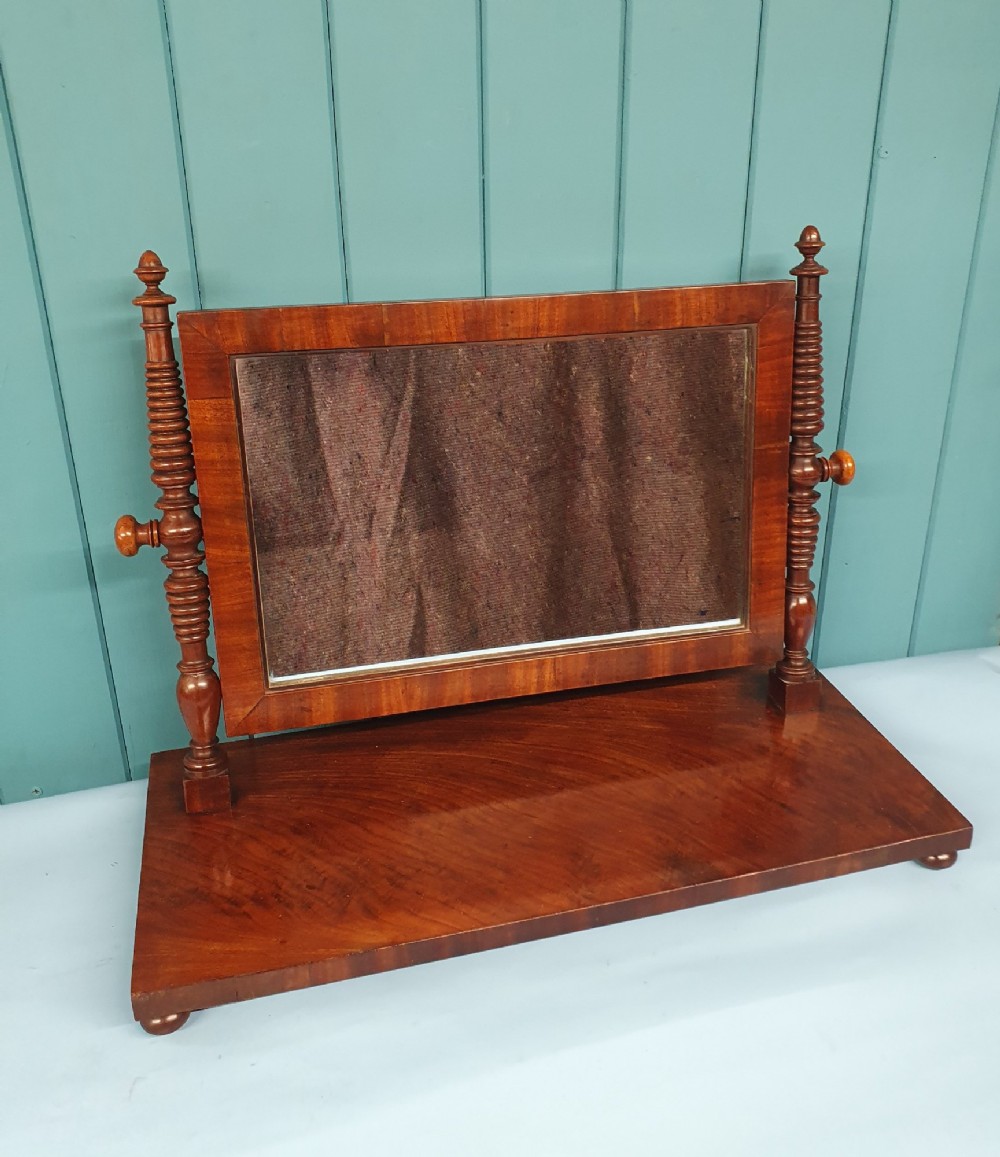 A 19th-century rectangular mahogany dressing mirror with turned side posts resting on a flat plinth base.