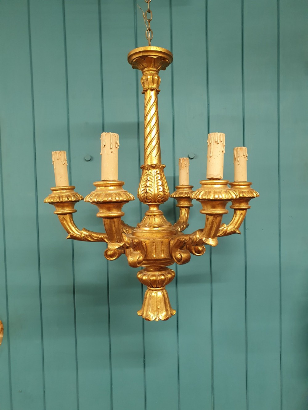 A Victorian circa 1890 six-arm giltwood chandelier featuring carved scroll arms, fluted details, and faux candle sleeves.