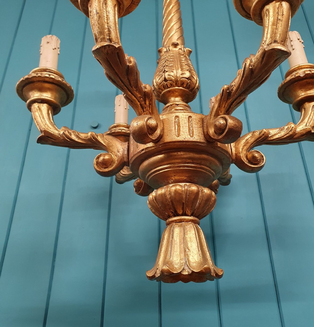 A Victorian circa 1890 six-arm giltwood chandelier featuring carved scroll arms, fluted details, and faux candle sleeves. View X