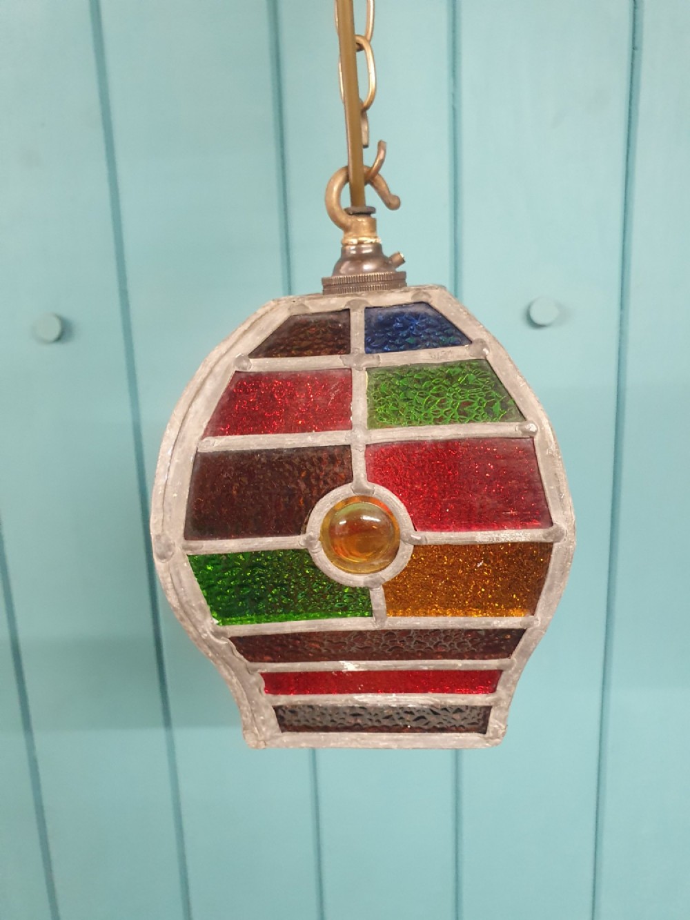 An early 20th-century leaded stained-glass porch lantern featuring geometric panels of red, green, amber, and blue glass with round glass cabochons, suspended from a brass chain. View II