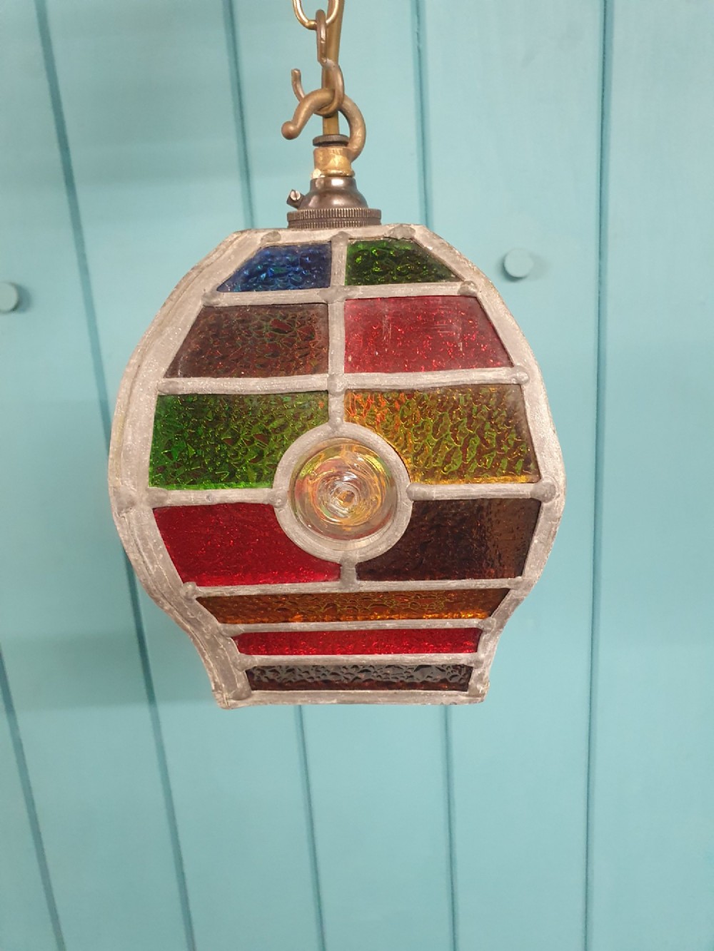 An early 20th-century leaded stained-glass porch lantern featuring geometric panels of red, green, amber, and blue glass with round glass cabochons, suspended from a brass chain. View III
