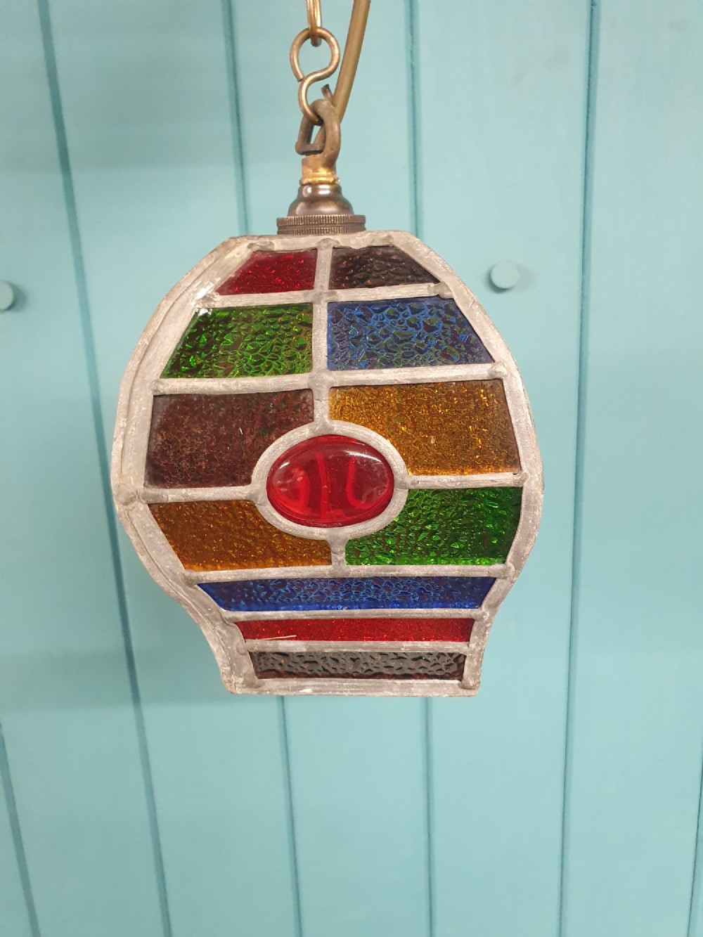 An early 20th-century leaded stained-glass porch lantern featuring geometric panels of red, green, amber, and blue glass with round glass cabochons, suspended from a brass chain. View IV