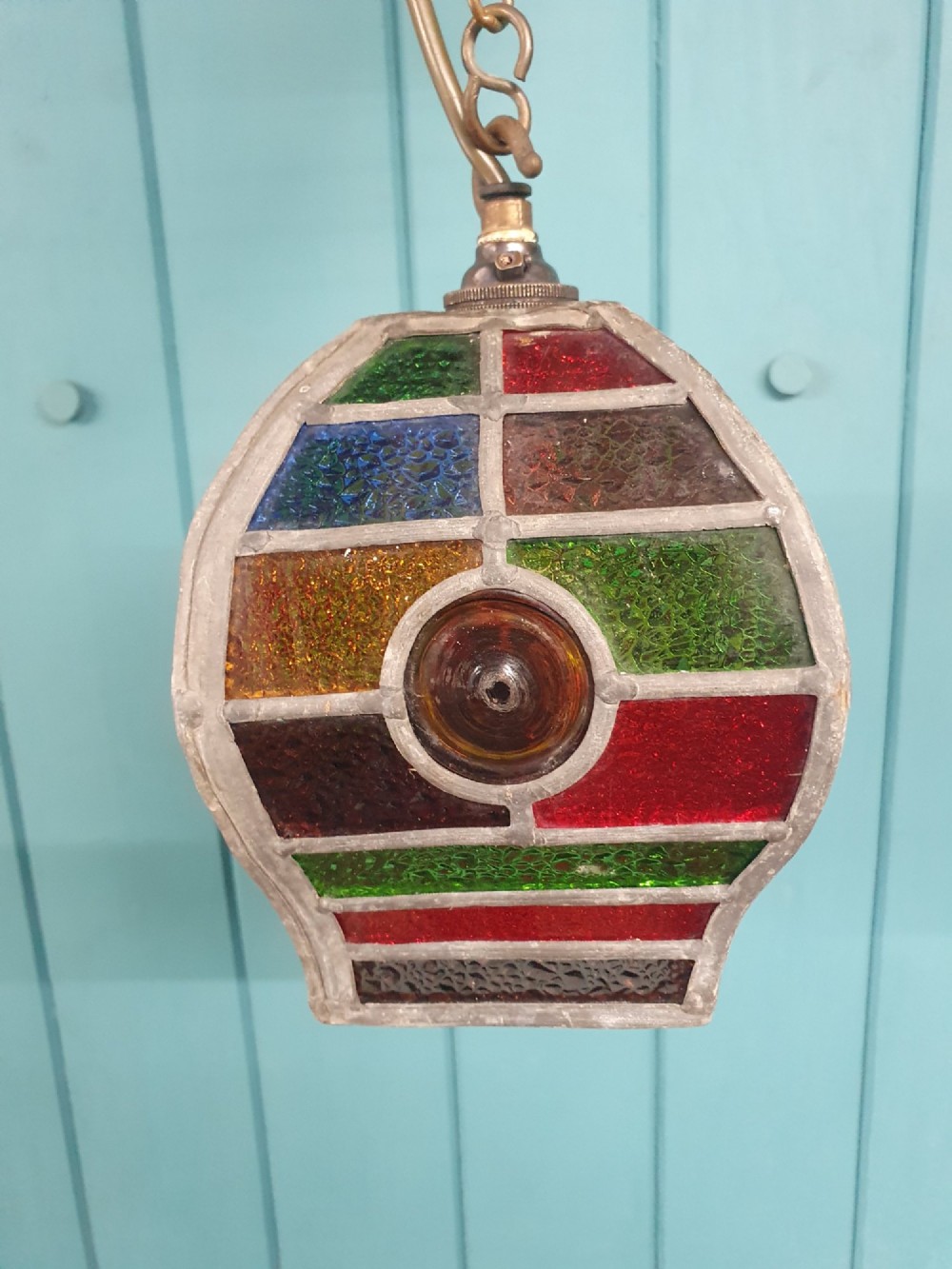 An early 20th-century leaded stained-glass porch lantern featuring geometric panels of red, green, amber, and blue glass with round glass cabochons, suspended from a brass chain. View V