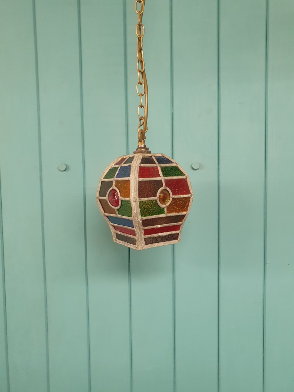 An early 20th-century leaded stained-glass porch lantern featuring geometric panels of red, green, amber, and blue glass with round glass cabochons, suspended from a brass chain.