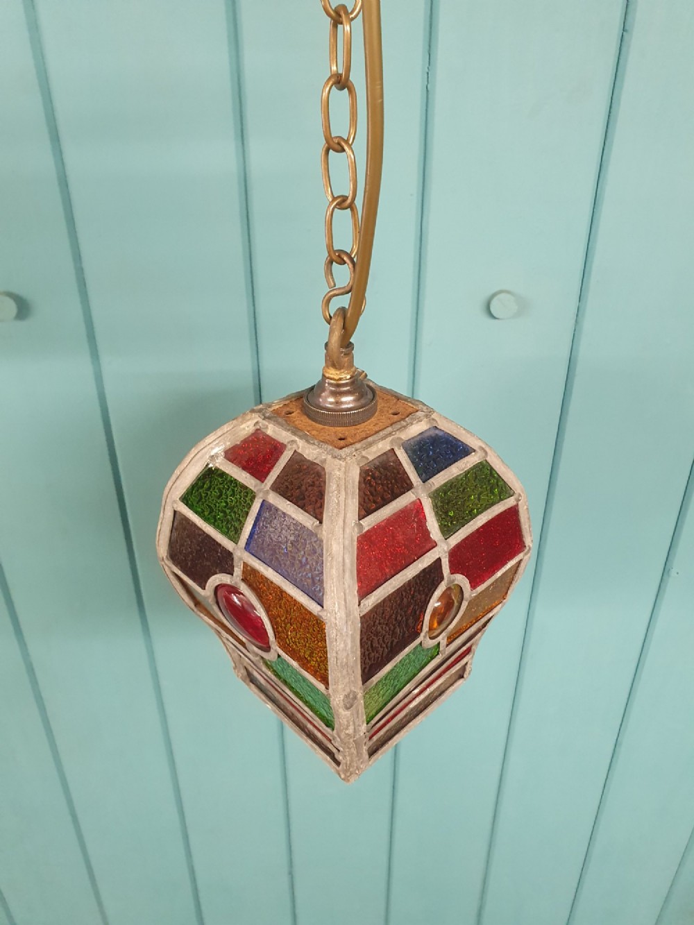An early 20th-century leaded stained-glass porch lantern featuring geometric panels of red, green, amber, and blue glass with round glass cabochons, suspended from a brass chain. View VI