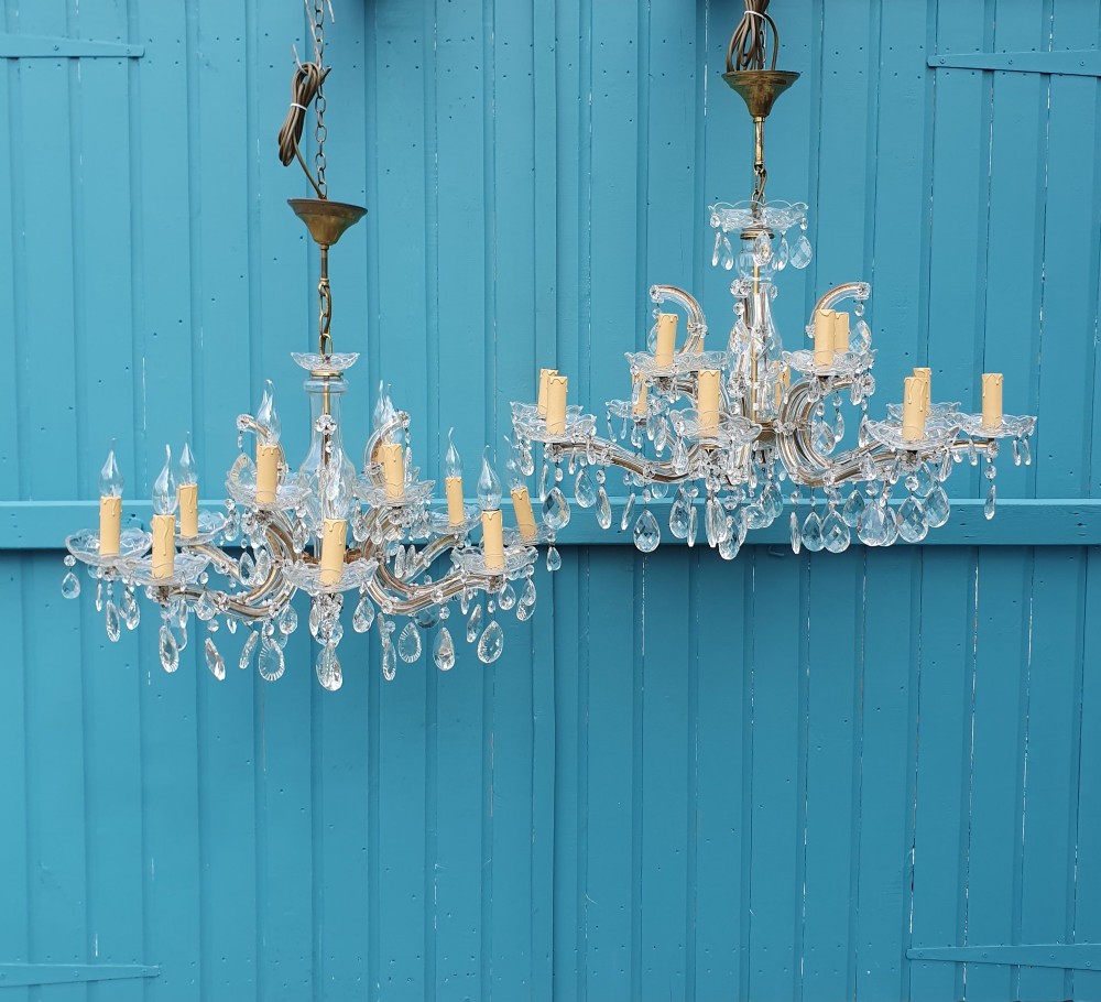 A matched pair of early 20th-century twelve-arm crystal chandeliers with faceted glass drops, curved arms, and brass mounts.