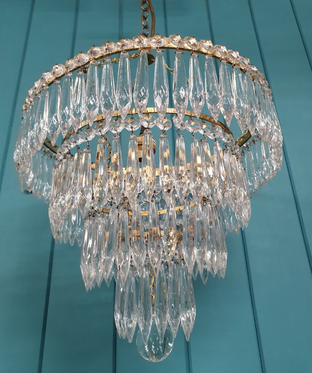 A tiered brass ceiling chandelier featuring multiple concentric rows of clear glass spike crystal prisms suspended by a chain. View II