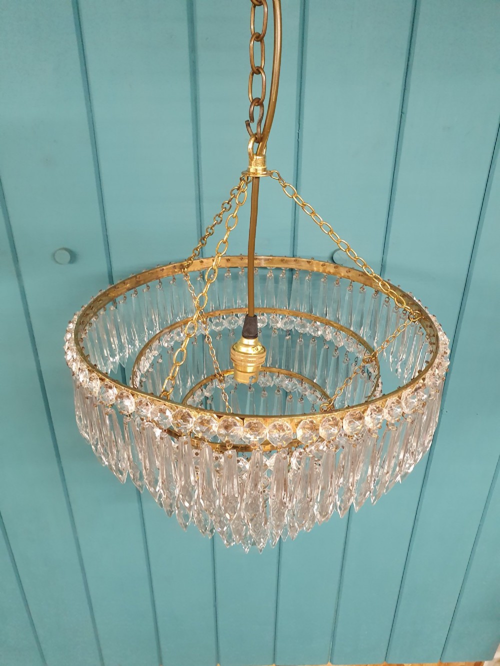 A tiered brass ceiling chandelier featuring multiple concentric rows of clear glass spike crystal prisms suspended by a chain. View III