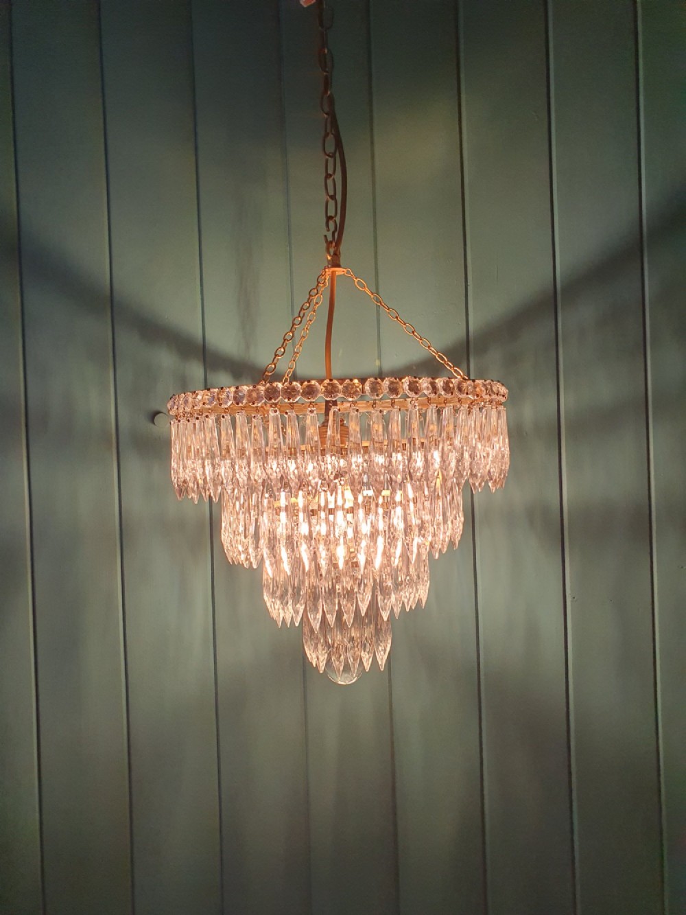 A tiered brass ceiling chandelier featuring multiple concentric rows of clear glass spike crystal prisms suspended by a chain. View IV